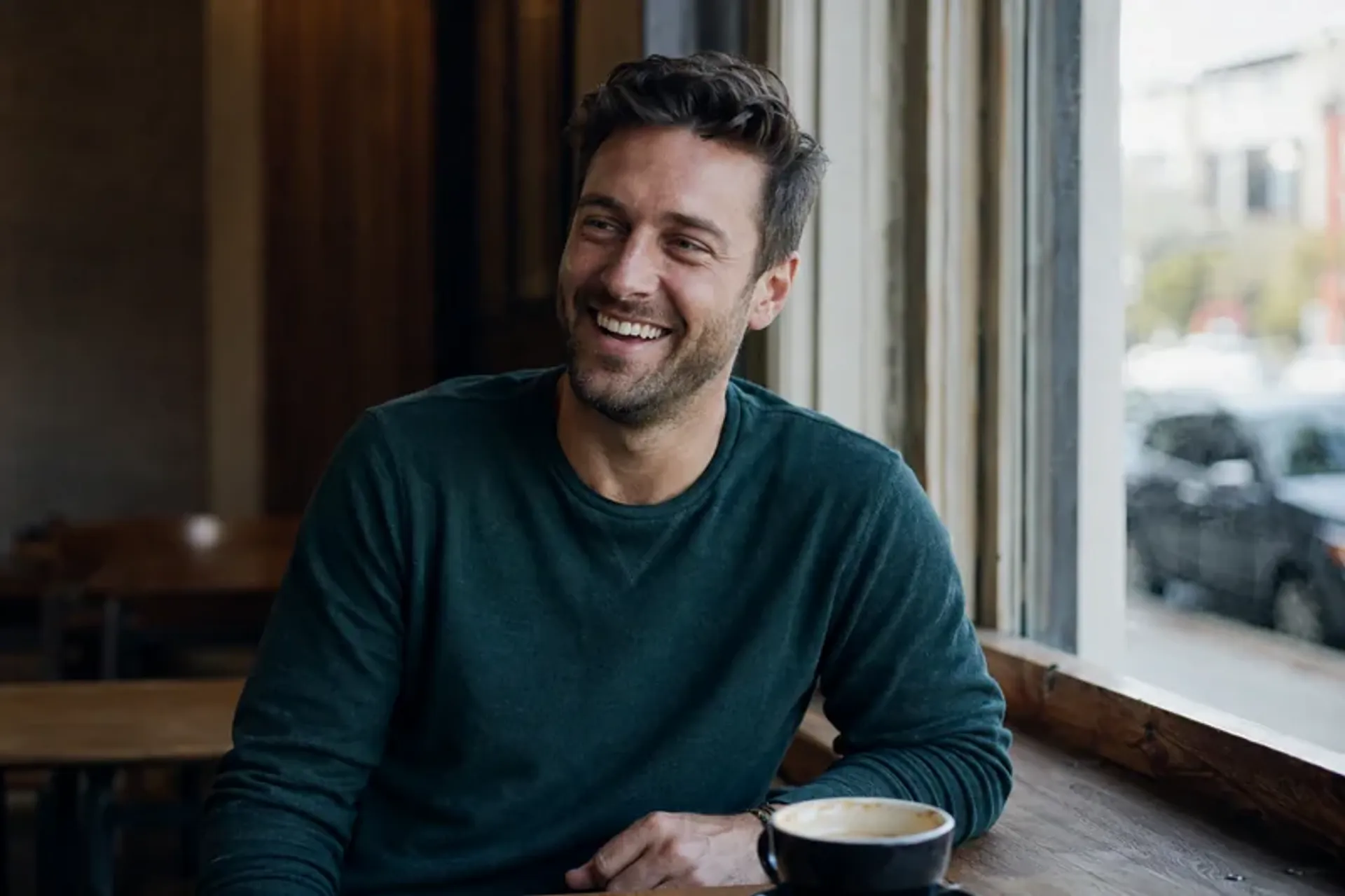 Man laughing naturally in a clear-face candid dating profile photo at a cafe