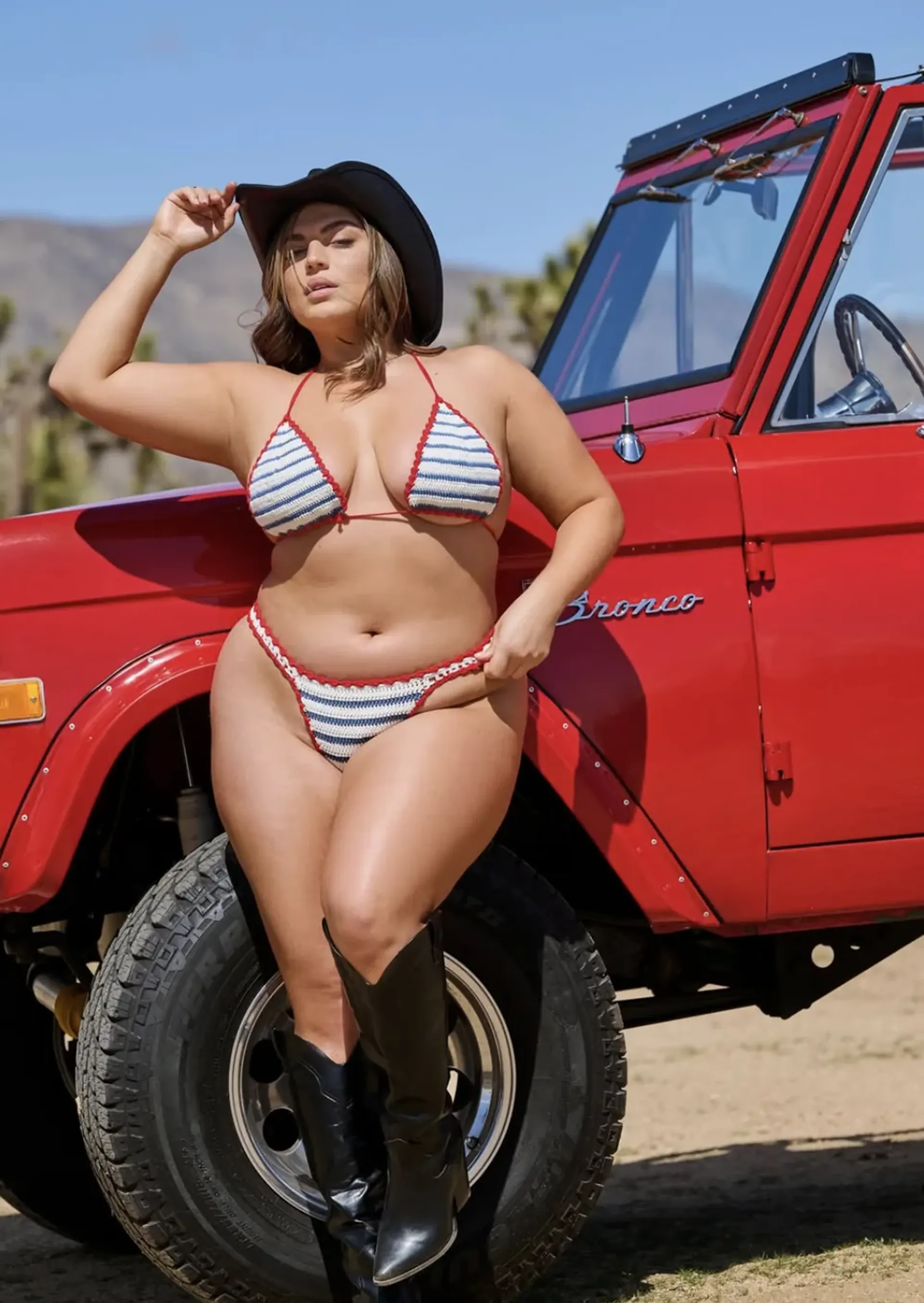 Nyome Nicholas-Williams posing in a striped bikini by a red car